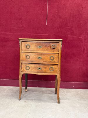 a small wooden chest of drawers on display in front of a red wall