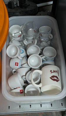 de nombreuses tasses et soucoupes dans un récipient posé par terre