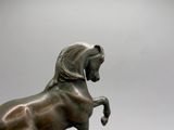 statue en bronze représentant un cheval, posée sur un socle en bois, sur fond gris
