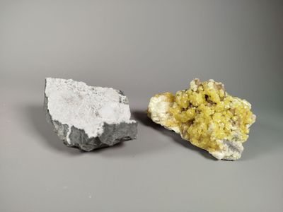 two pieces of yellow and white mineral on a gray surface