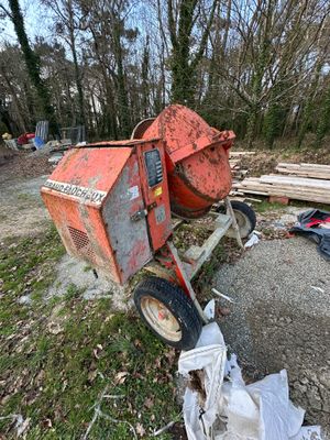 a cement mixer sitting on the ground next to a pile of wood