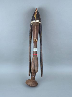 une vieille statue en bois représentant un homme aux cheveux longs et coiffé d'un chapeau