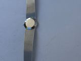 a silver watch on a table with a coin on it