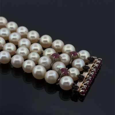 un collier de perles posé sur un fond noir, orné d'une broche rouge et blanche