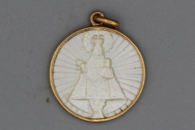 une image représentant un pendentif blanc et doré sur lequel figure une femme tenant un enfant dans ses bras