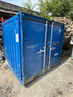 un conteneur bleu posé dans la terre à côté d'un tas de bois