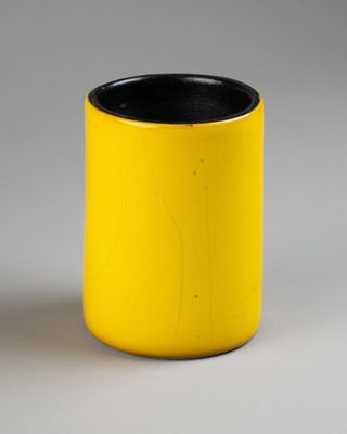 une tasse jaune à bord noir posée sur une surface blanche