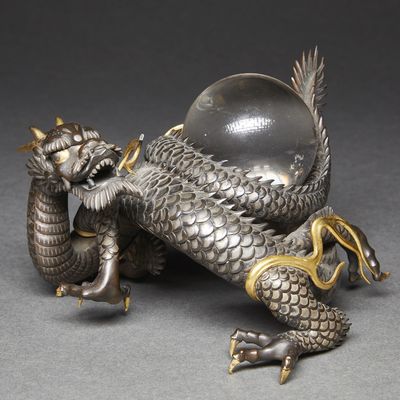 an antique silver dragon figurine with a glass ball on its back