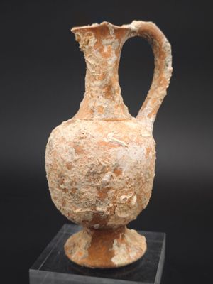 un vieux vase muni d'une anse est posé sur un socle transparent