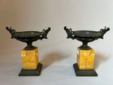 pair of black and gold urns on marble pedestals on a white background