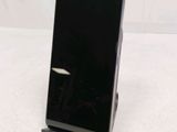 a black cell phone sitting on a stand on a white surface