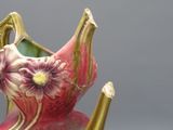 un vase rose avec une anse jaune et une fleur dessus