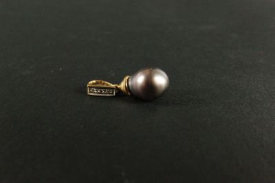 un pendentif en forme de perle argentée muni d'un fermoir en or, sur un fond noir
