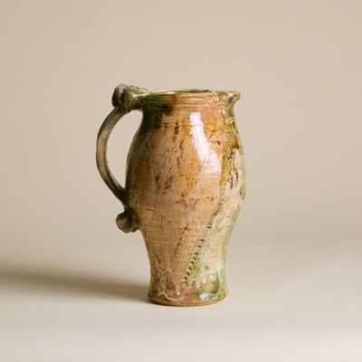 un vase marron et vert posé sur une surface blanche
