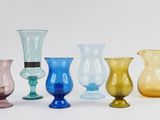 several different colored glass vases are lined up on a white surface