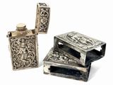 three antique silver lighters with ornate designs on them on a white surface
