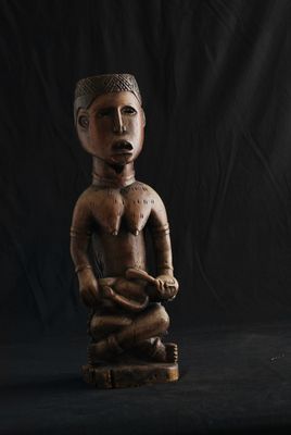 une vieille statue en bois représentant un homme tenant un serpent, sur fond noir
