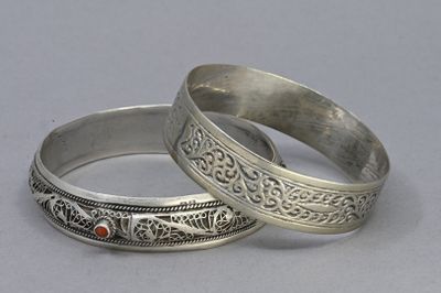 pair of silver bangles with red stones on them on a gray surface