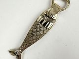 silver fish shaped bottle opener with a metal handle on a white surface