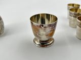 four silver cups and a silver spoon on a white surface