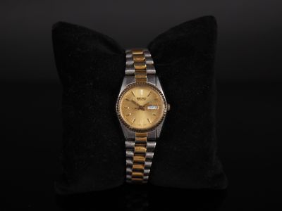 a gold and silver watch sitting on top of a black pillow