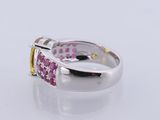 a close up of a ring with pink and yellow stones on a white surface