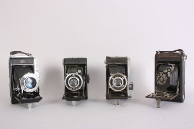 three old cameras sitting side by side on a white surface
