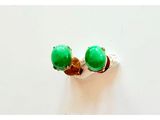 une paire de boucles d'oreilles à clous ornées de pierres vertes, posées sur une surface blanche