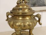 a large brass incense pot on a stand with a picture on the wall in the background