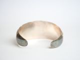silver cuff bracelet with a green stone in it on a white surface