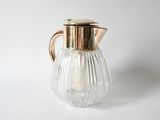 a glass pitcher with a gold lid on a white surface