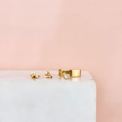 a pair of gold and diamond stud earrings sitting on top of a marble block
