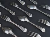 a lot of silver spoons and forks on a black table