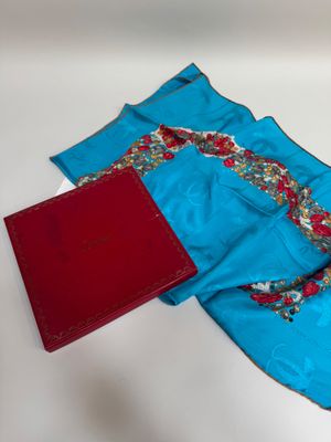une écharpe bleue et un livre rouge posés sur une table blanche