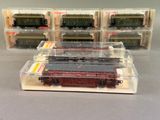Plusieurs trains miniatures sont posés dans des boîtes transparentes sur une table