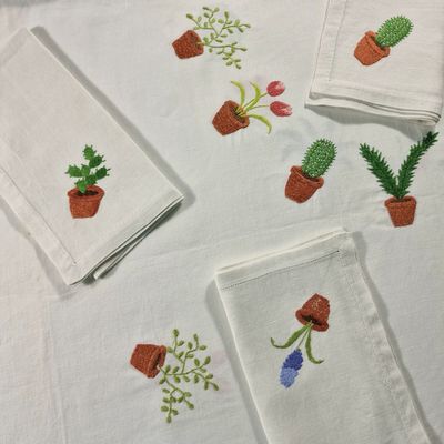 des serviettes brodées représentant des plantes en pot, posées sur une table