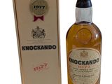 une bouteille de whisky Knockandoo posée à côté d'un carton