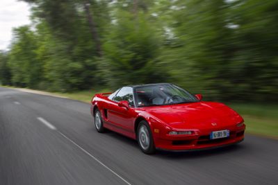 a red sports car driving down the road with trees in the background