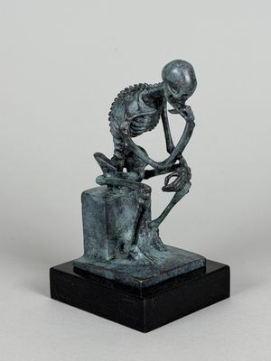 bronze statue of a skeleton sitting on a rock with his head in his hands