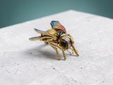 gold plated bee brooch with multicolored wings on a white surface