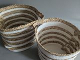 two white and brown woven baskets with handles on a table