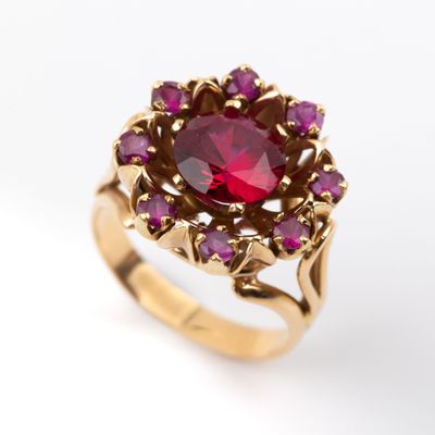 une image représentant une bague en or sertie d'une pierre rouge entourée de pierres violettes