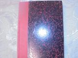un cahier rose et noir posé sur une table blanche