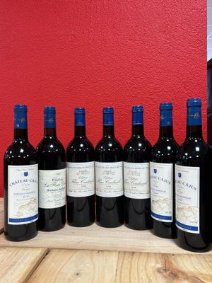 six bottles of red wine lined up on a wooden table