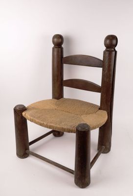 wooden chair with rope seat and back rest against a white wall