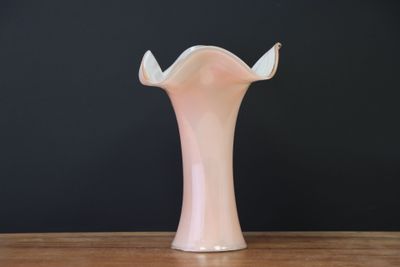 un vase rose posé sur une table en bois, avec un mur noir en arrière-plan