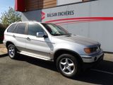 Une BMW X5 garée devant un immeuble arborant le logo de Balean Encheres