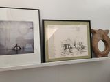 two framed pictures on a shelf above a toilet