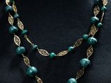 un collier composé de perles vertes et de feuilles dorées, présenté sur un mannequin