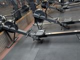 row of rowing machines in a gym with mirrors on the wall
